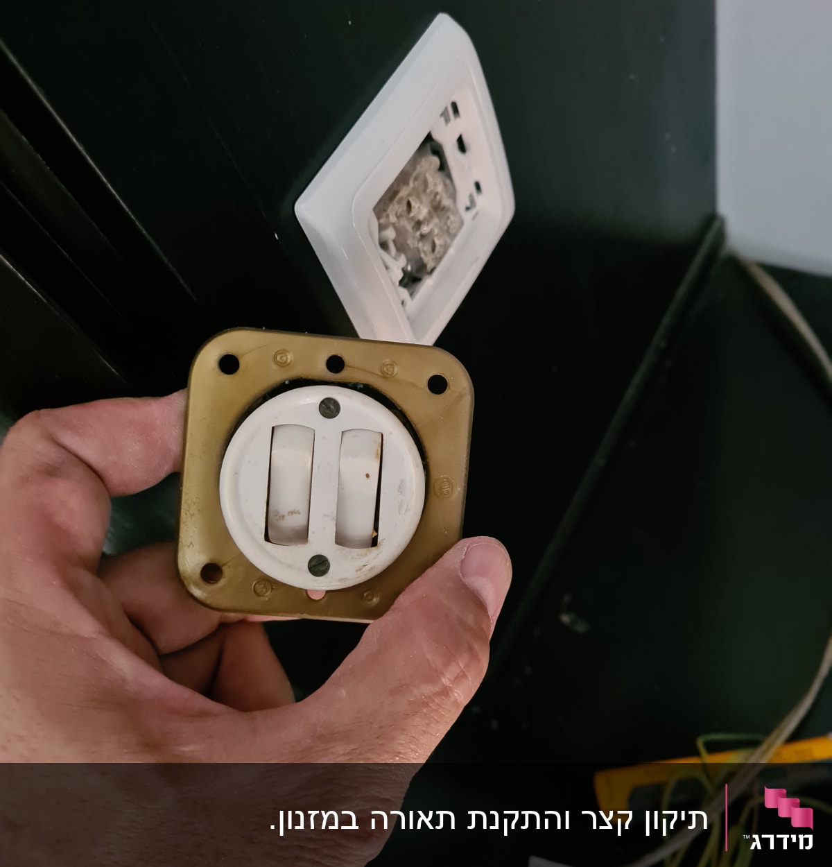 יד מחזיקה מתג חשמלי ישן ליד שקע פתוח בקיר